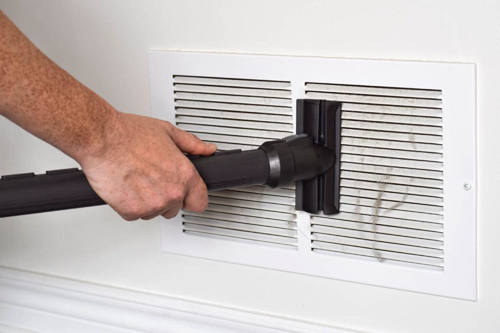 Cleaning pro vacuums a dusty air vent during air duct cleaning.